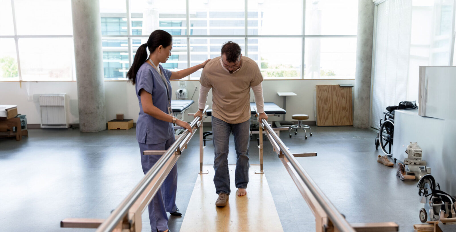 A mid adult female nurse helps a mid adult patient maintain stability while walking for the first time after foot surgery.